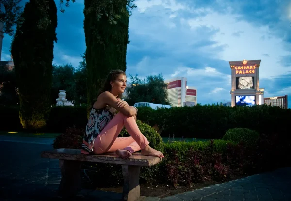 Las Vegas Strip senior portraits senior girl in peach pants sitting outdoors near Caesars Palace at dusk