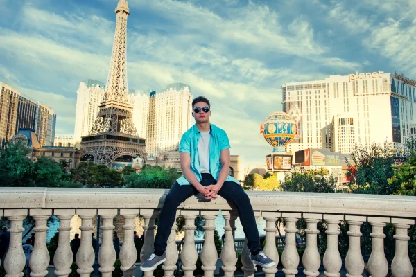 Las Vegas Strip senior portraits senior guy sitting on a railing with the Paris Las Vegas Eiffel Tower in the background