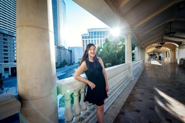 Las Vegas Strip senior portraits senior girl in a black dress posing on a Bellagio balcony with sun flare