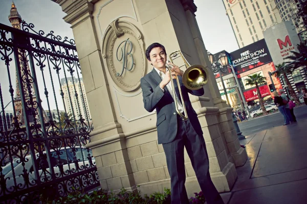 Las Vegas Strip senior portraits senior guy in a suit playing trombone near a gated entrance on the Strip